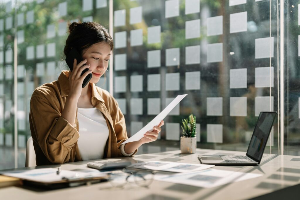 Young asian accountant calling marketing consultants and using laptop computer to analyze sales